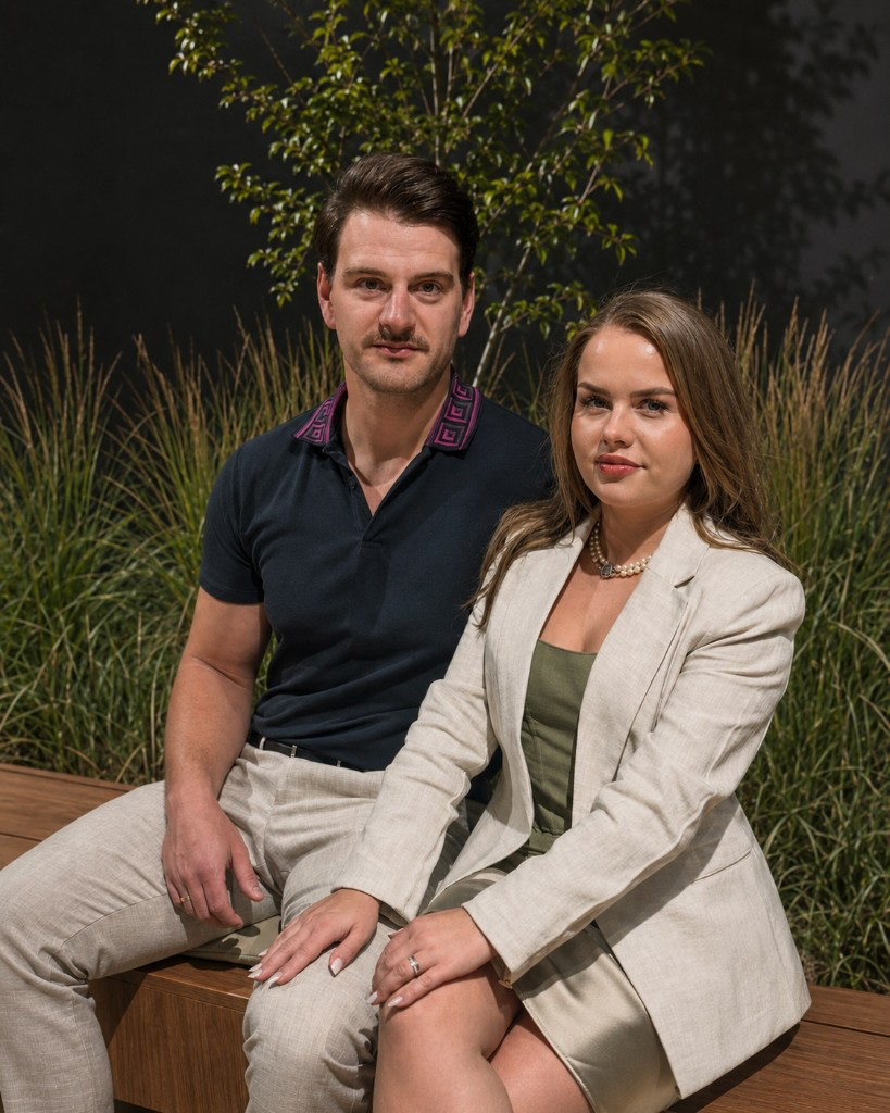 Adriana und Lukas von ZILA GLANZ – Portrait auf einer Holzbank mit Grün und dunklem Hintergrund; Team für Premium-Objektpflege in Tirol.